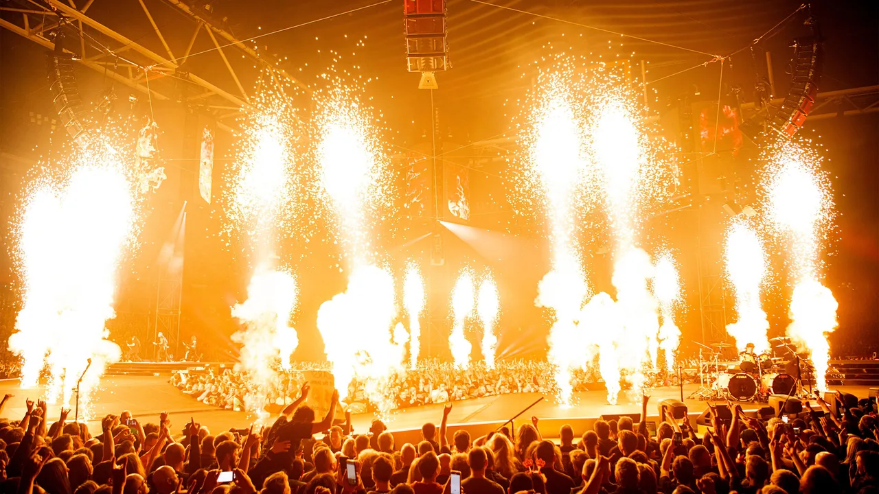 Banda de heavy metal se apresentando em um palco com luzes intensas e pirotecnia