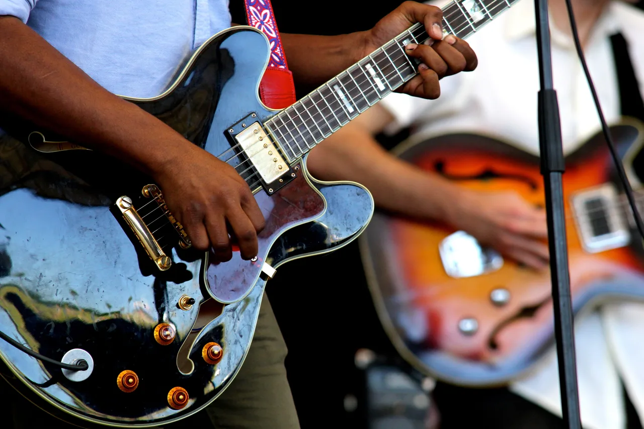 Guitarrista tocando guitarra elétrica, com as mãos no braço do instrumento